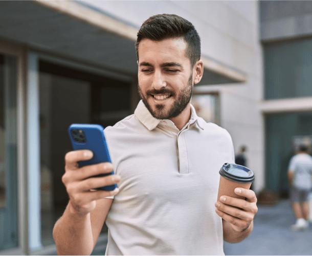 Smiling man holding a coffee cup and checking his smartphone