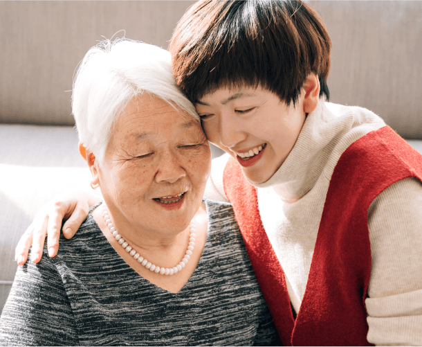 Smiling younger woman embracing her elderly mother, representing family support and senior care